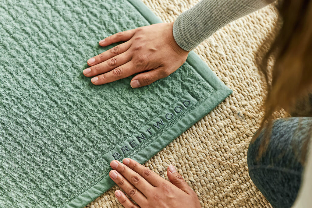 Close-up photo of someone's hands resting on the edge of a yoga mat. Physical self care can also help reduce stress—and improve sleep.
