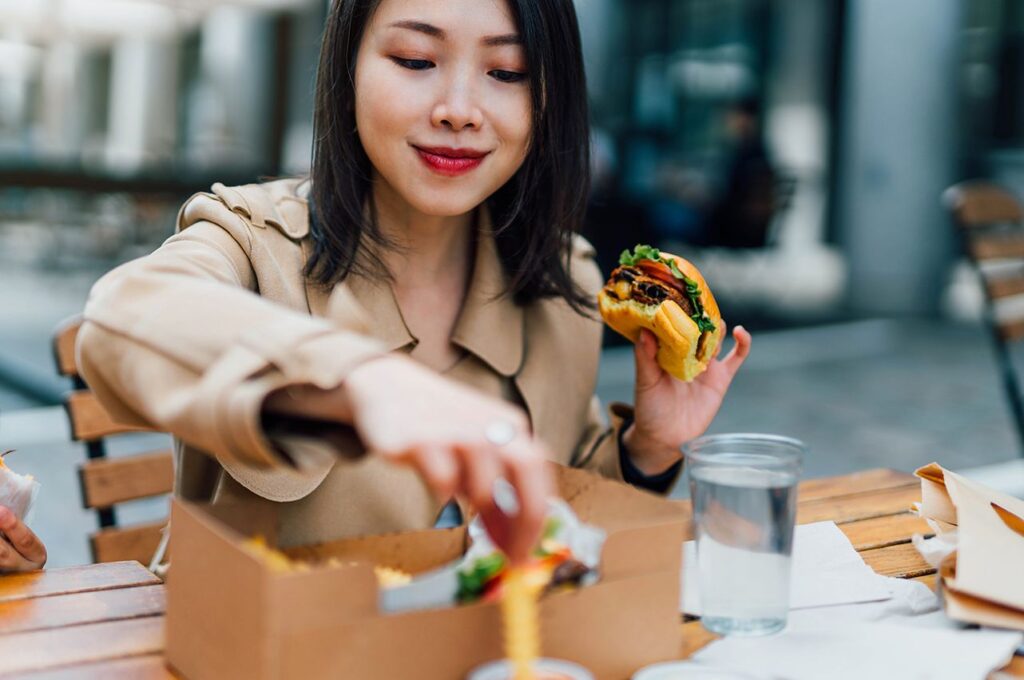 A woman dines outside holding a burger and fries