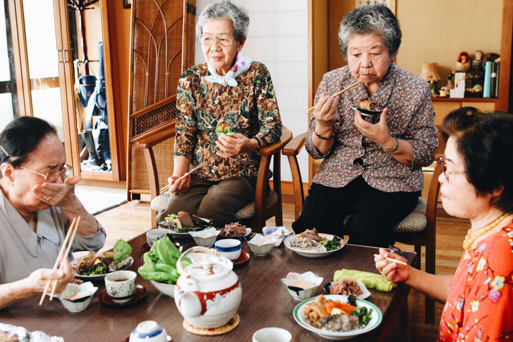 Photo shows a group of Okinawan women eating a traditional lunch together around a low table. One of the most commented-upon benefits of a flexitarian diet is increased longevity.