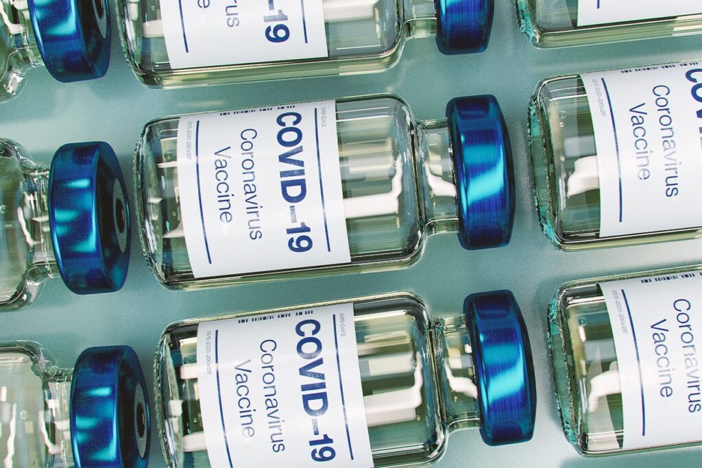 Photo shows glass vials of the COVID-19 vaccine lined up on a green background.