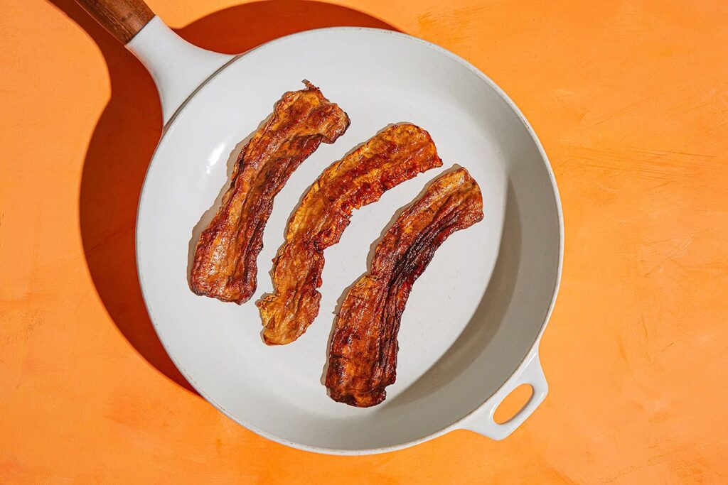 Photo shows three pieces of mycelium-based bacon on a skillet