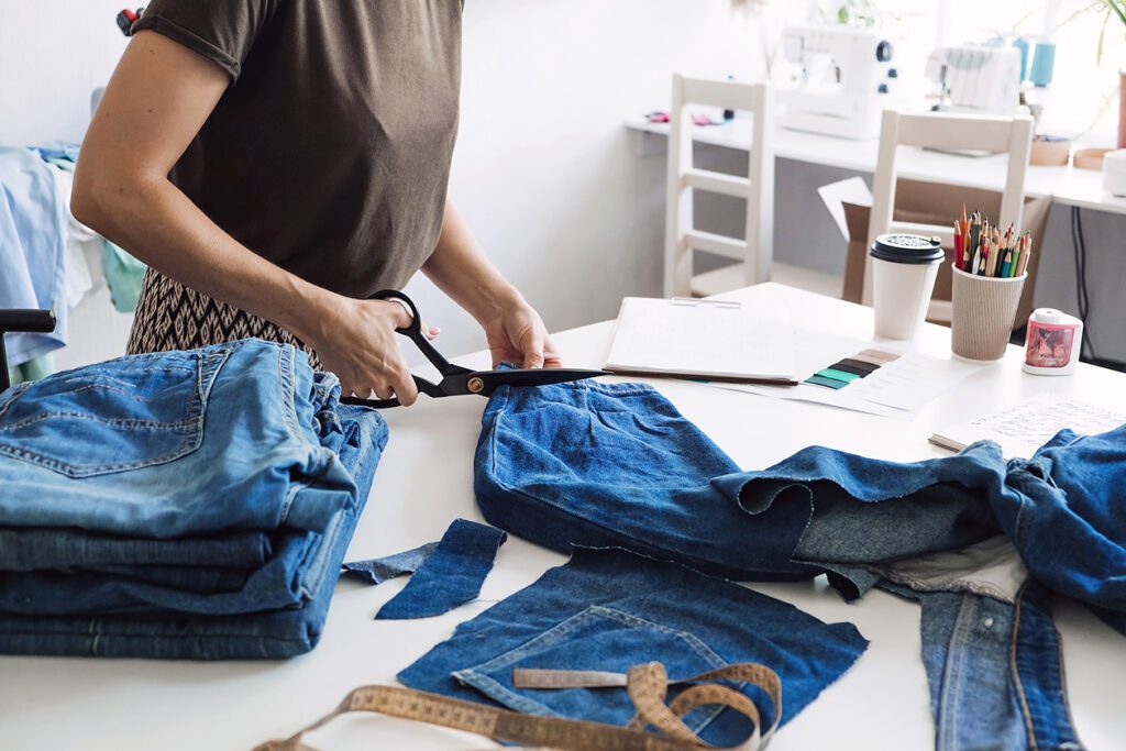Photo shows someone cutting up a pair of blue jeans with large scissors in order to reuse the fabric.